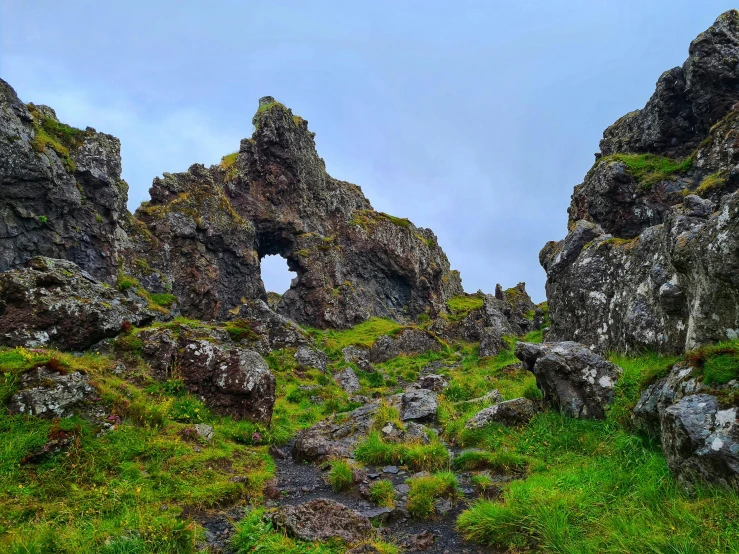 a group of rocks sitting on top of a lush green hillside, by Þórarinn B. Þorláksson, pexels contest winner, art nouveau, an archway, devils horns, marble hole, thumbnail