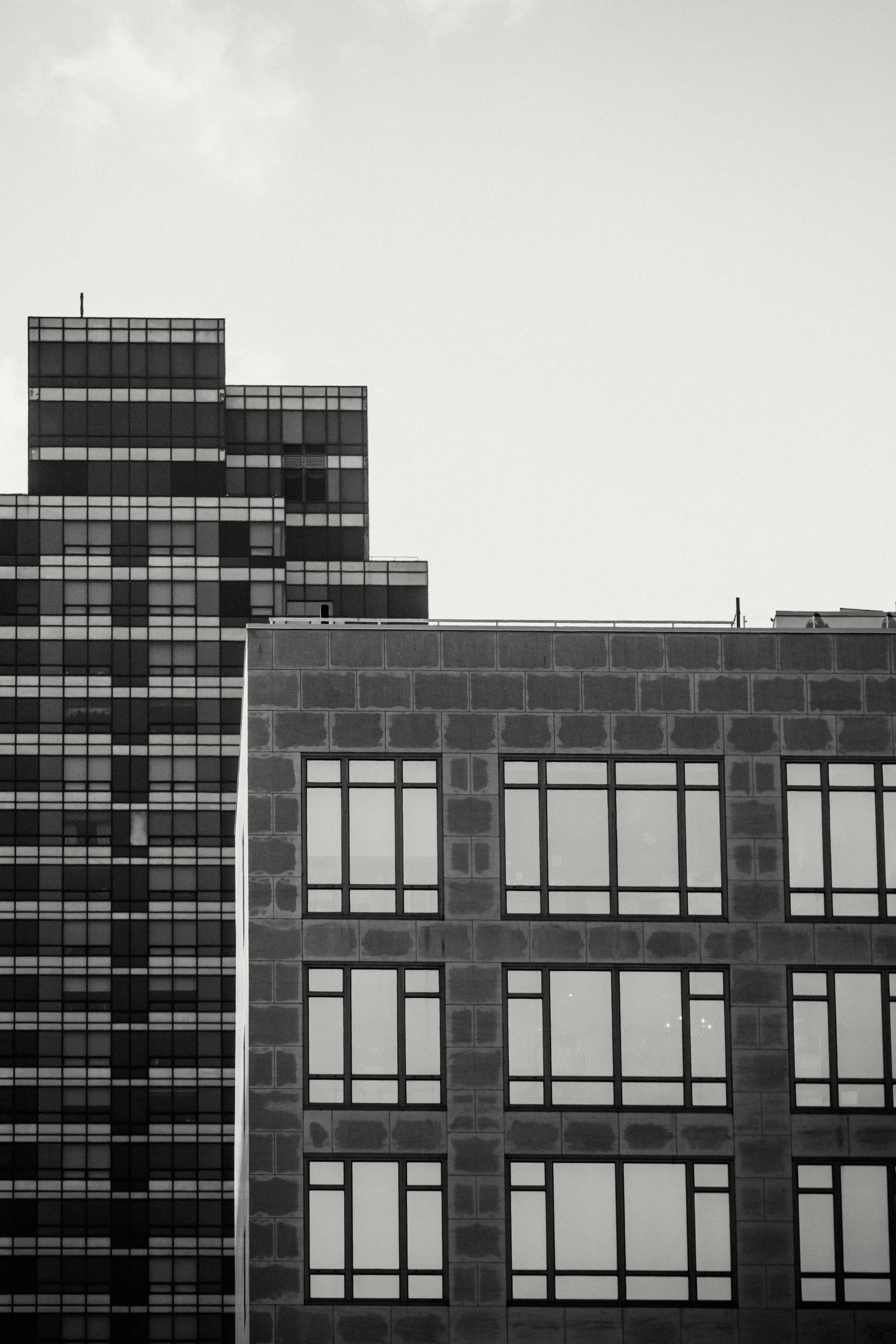 a black and white photo of a tall building, a black and white photo, unsplash, brutalism, other smaller buildings, house windows, two towers, color contrast