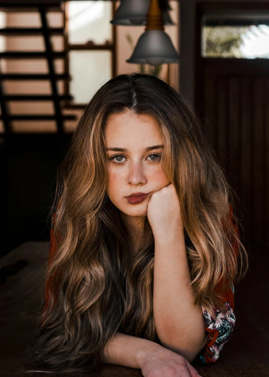 a beautiful young woman laying on top of a wooden table, a picture, by Winona Nelson, trending on pexels, joey king, square, looking serious, long wavy brown hair