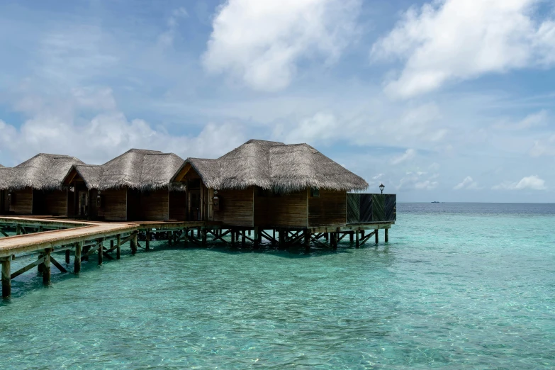 a group of huts sitting on top of a body of water, trending on unsplash, hurufiyya, clear blue skies, holiday resort, 2000s photo, multiple stories