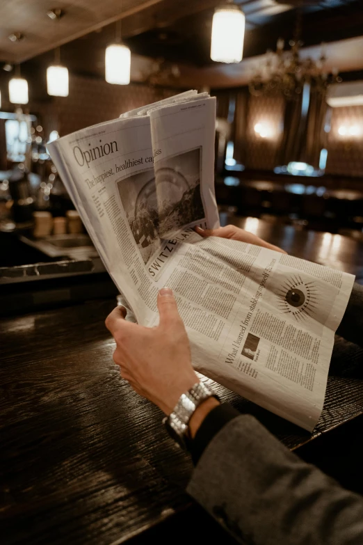 a man sitting at a bar reading a newspaper, unsplash, private press, holding it out to the camera, thumbnail, ap news photograph, covered in