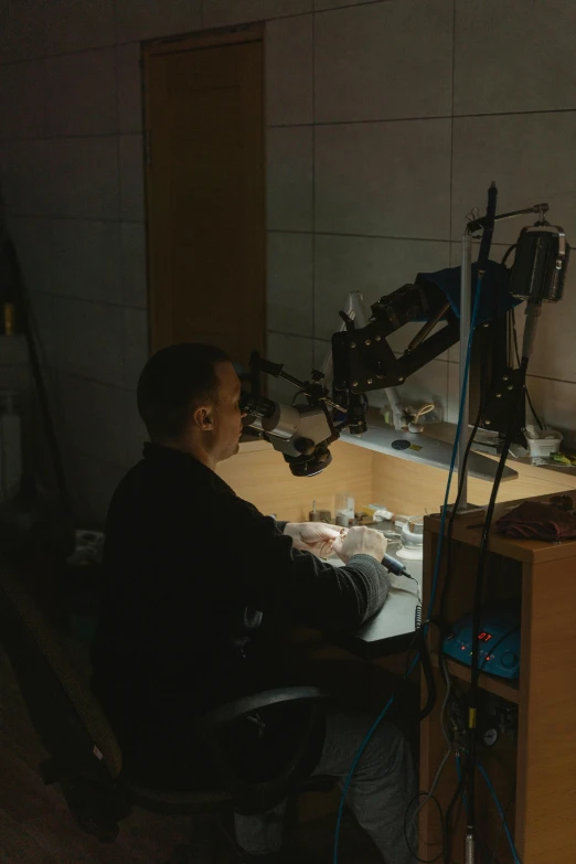 a man sitting at a desk in front of a computer, inspired by Jakub Husnik, holography, robot repair workshop, jewelry lighting, under studio lighting, 35mm —w 1920 —h 1080