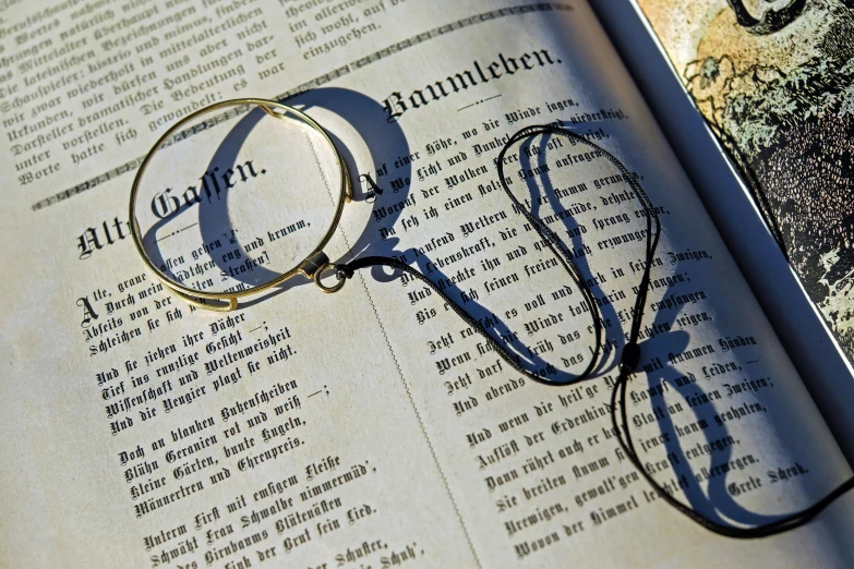 a pair of glasses sitting on top of an open book, hook as ring, in the sun, black and gold wires, behaelterverfolgung