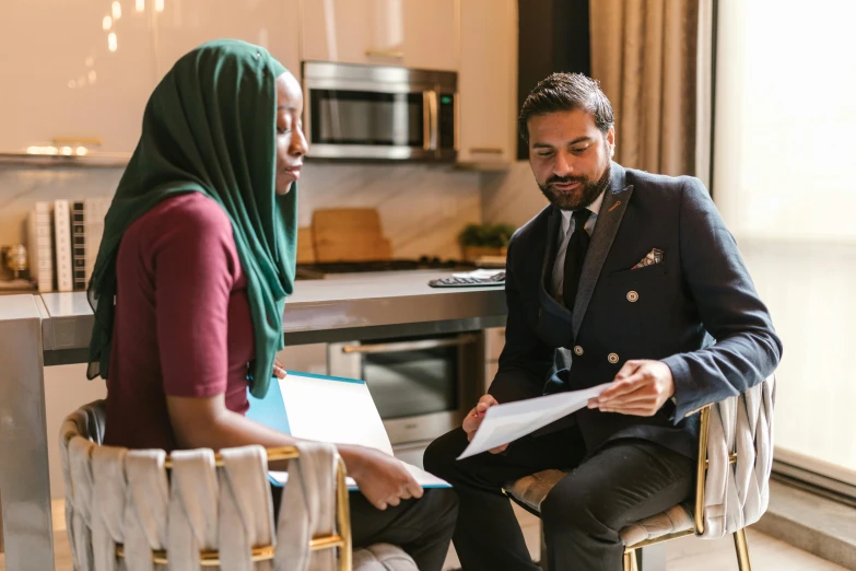 a man and a woman sitting in chairs in a kitchen, pexels contest winner, hurufiyya, selling insurance, charts, aida muluneh, profile image