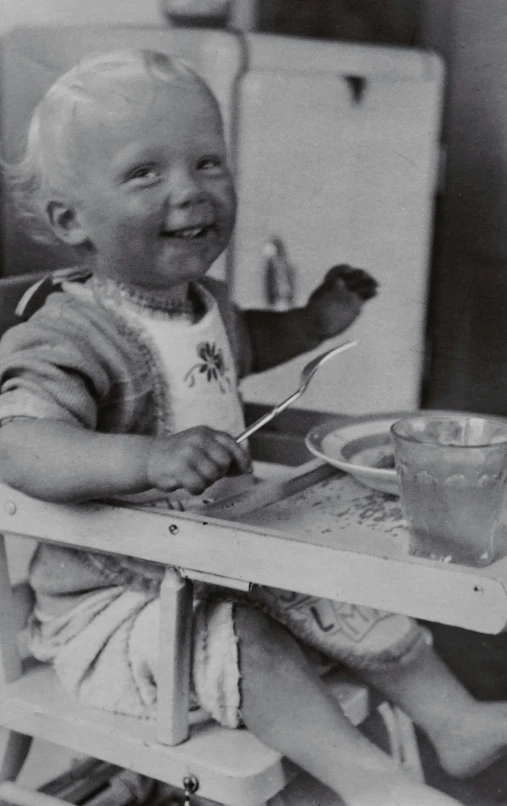 a black and white photo of a baby in a high chair, by Eero Järnefelt, smiling slightly, closeup at the food, historical footage, digital image