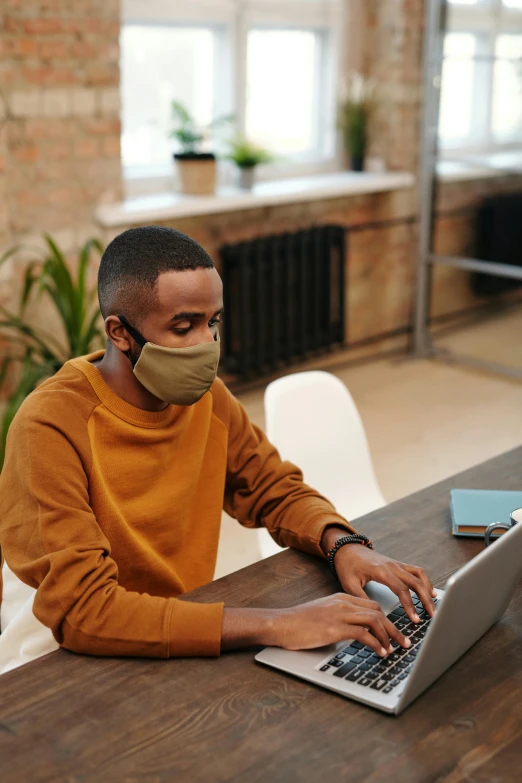 a man sitting at a table with a laptop wearing a face mask, trending on pexels, he is wearing a brown sweater, ashteroth, thumbnail, ap news