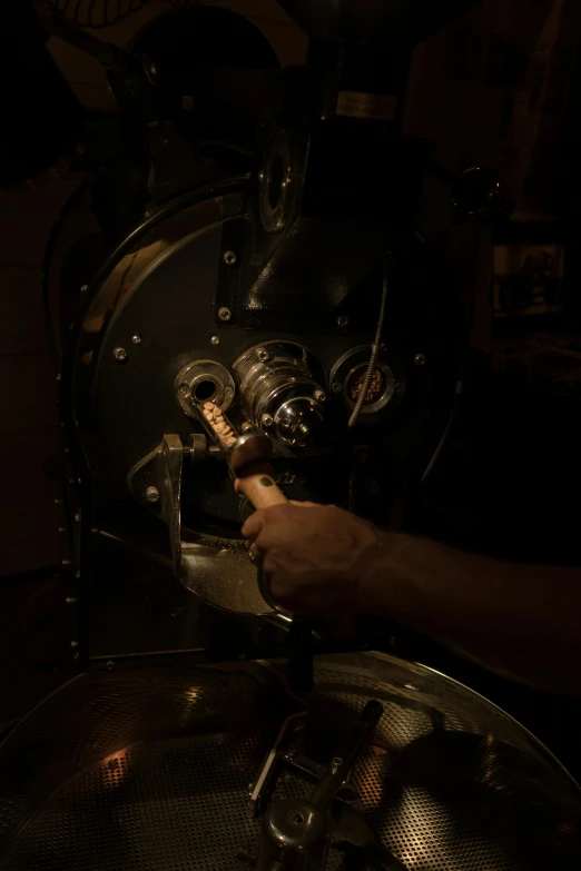 a person operating a coffee grinder in a dark room, process art, engine room, brown, woodfired, vanilla