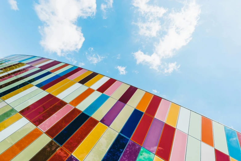 a multicolored building with a blue sky in the background, a mosaic, inspired by Jodorowsky, unsplash, color field, iron cladding, instagram post, coventry city centre, rainbow clouds