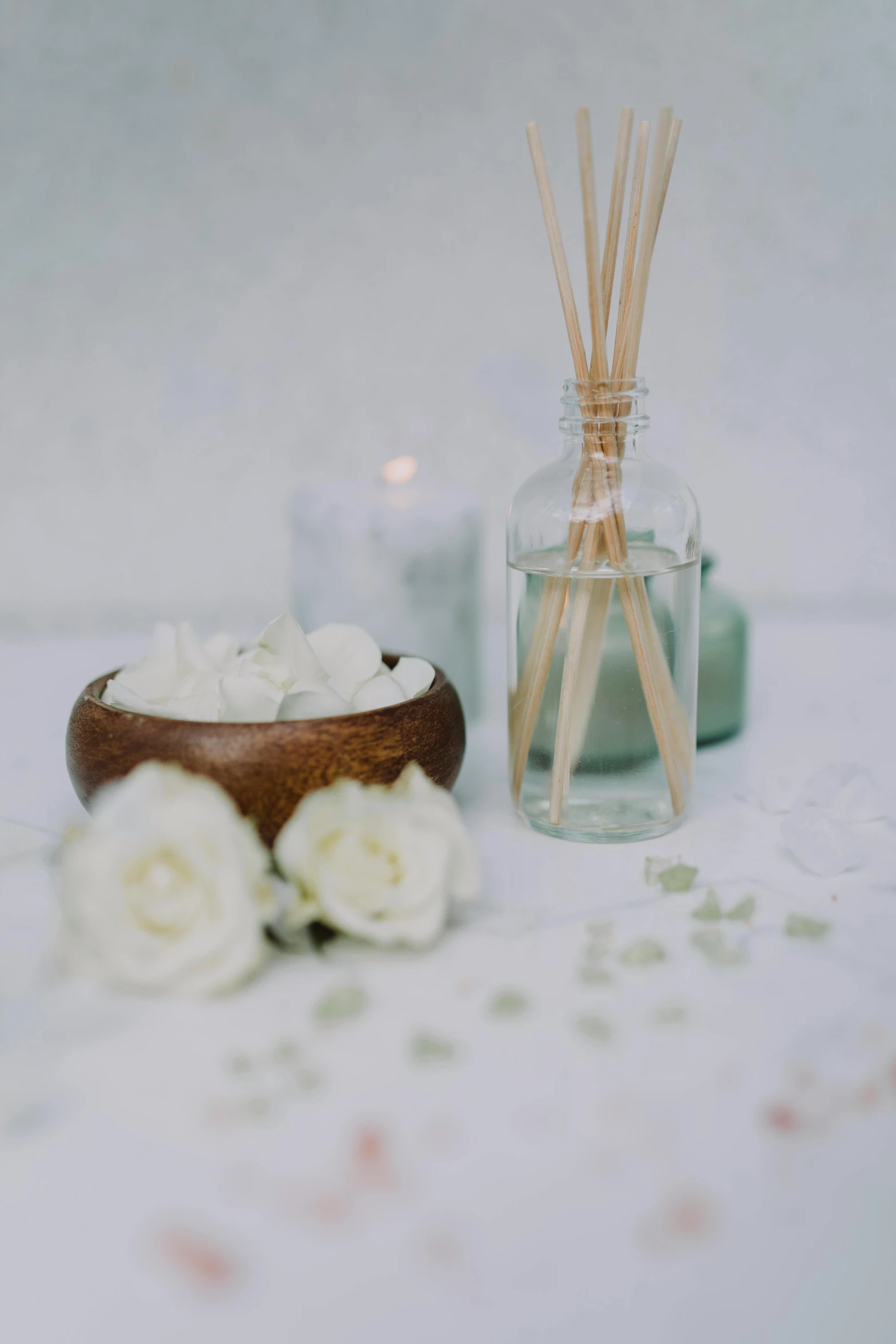 a wooden bowl sitting on top of a table next to a candle, a still life, unsplash, white roses, vapor, spa, in a white boho style studio