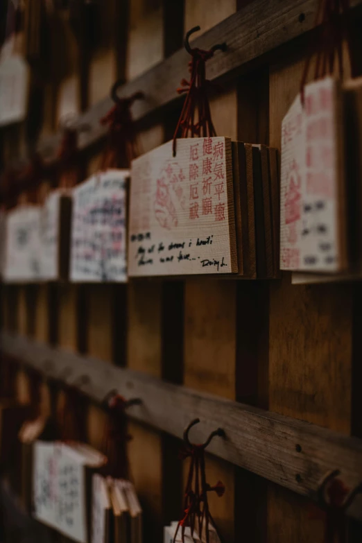 a number of tags attached to a wooden wall, a picture, inspired by Sesshū Tōyō, trending on unsplash, standing in a buddhist temple, with some hand written letters, cinematic still, facing sideways