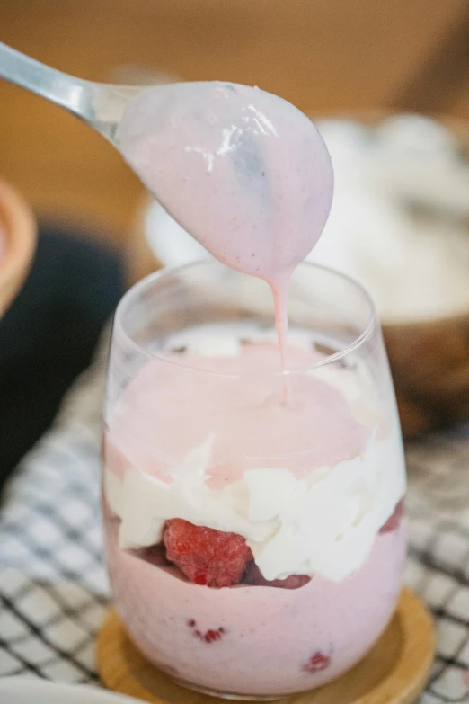 a close up of a bowl of food with a spoon, white and pink, glass of milk, raspberry, pouring
