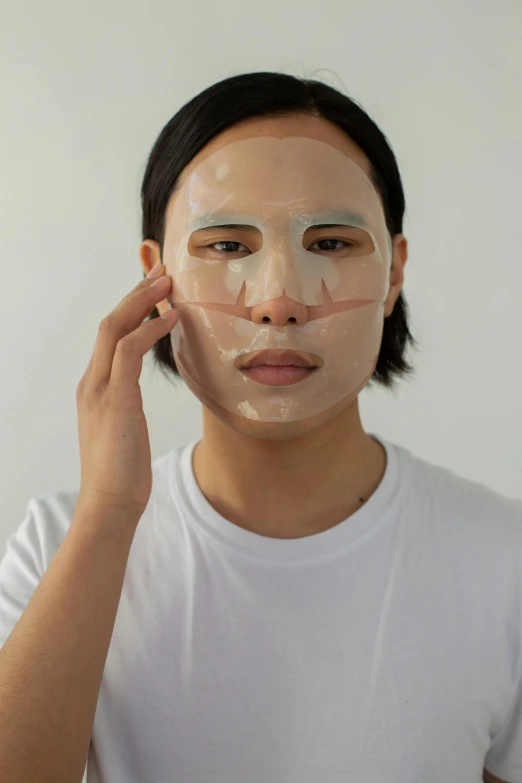 a man is putting a mask on his face, inspired by jeonseok lee, wearing translucent sheet, silicone skin, on clear background, androgynous face