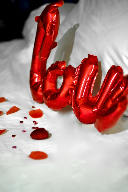 a red love balloon laying on top of a bed, foil, lots de details, zoom shot, pillows