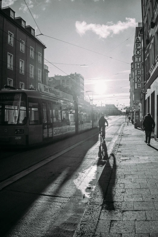 a man riding a bike down a street next to tall buildings, a black and white photo, by Tobias Stimmer, pexels contest winner, trams, sun glare, helsinki, photograph of the city street