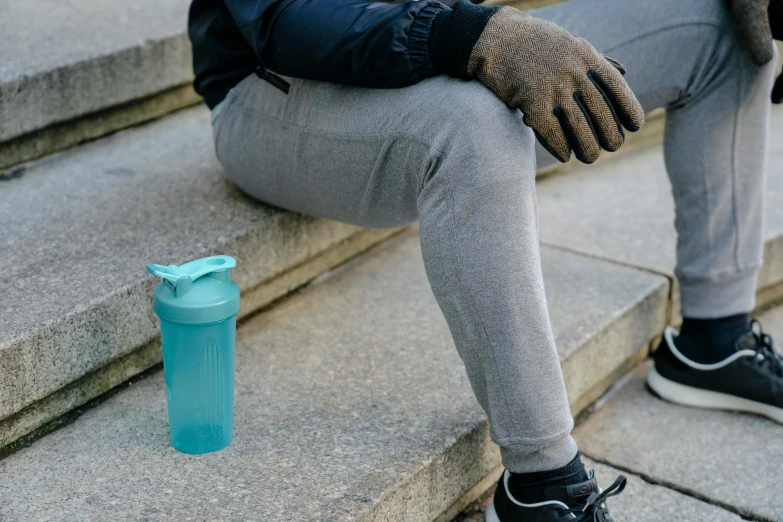 a man sitting on steps next to a water bottle, inspired by Kanō Tan'yū, trending on pexels, turquoise, grey, detail shot, frosty