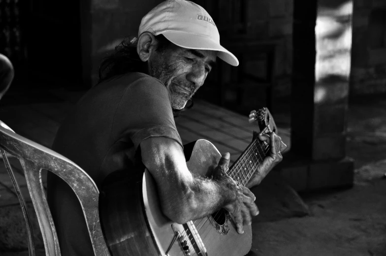 a man sitting on a chair playing a guitar, a black and white photo, by Mike Bierek, pexels contest winner, peruvian looking, smiling man, don ramon, shaded