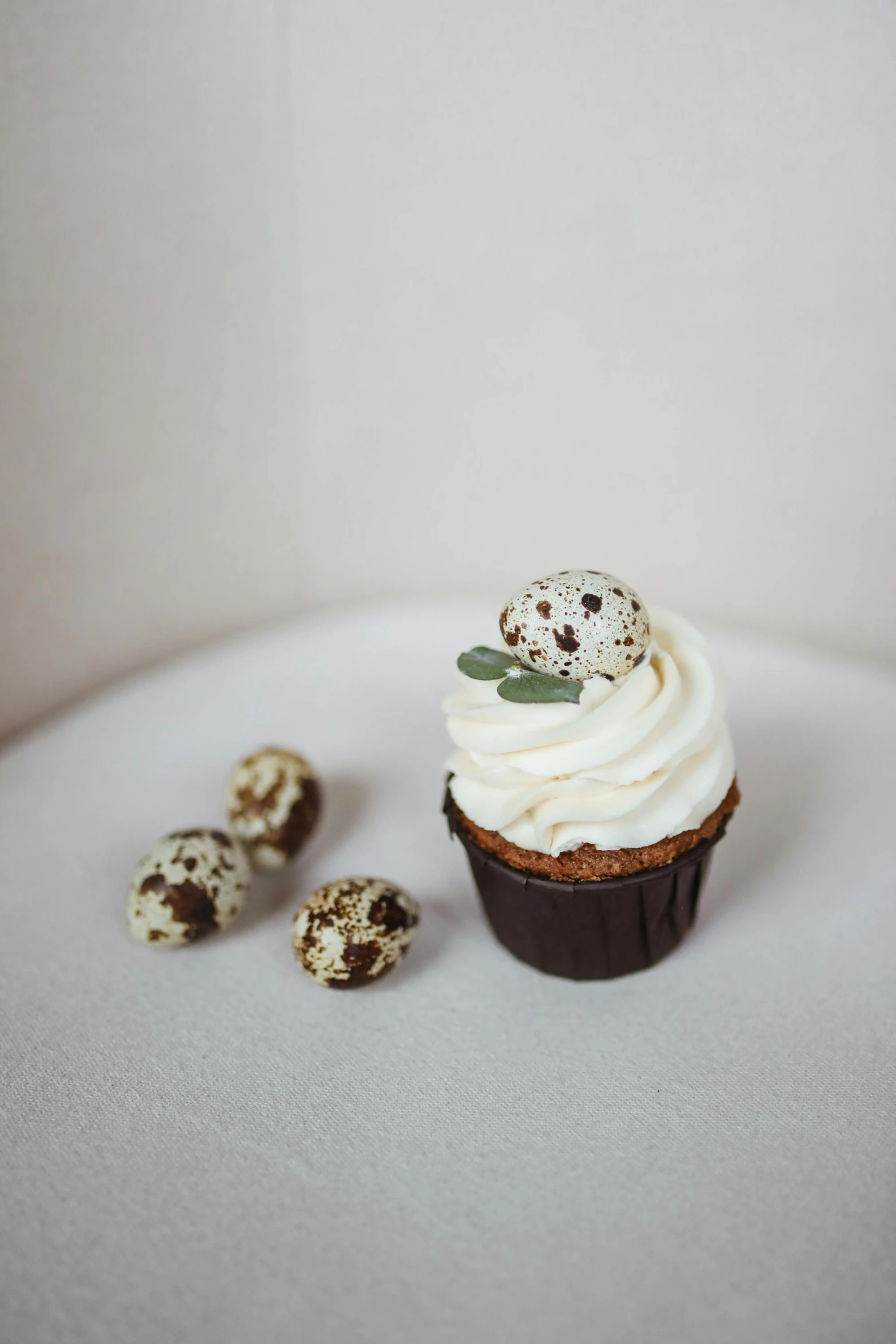 a cupcake sitting on top of a white plate, ornate egg, eucalyptus, white with chocolate brown spots, detailed product shot