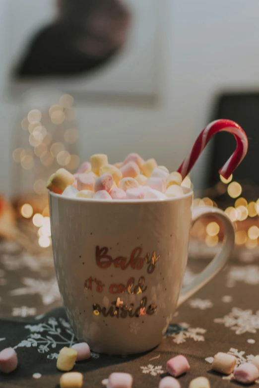 a cup of hot chocolate with marshmallows and candy cane, by Alexander Brook, pexels, soft lights, gif, birth, gold