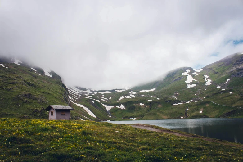 a small cabin sitting on top of a lush green hillside, by Sebastian Spreng, pexels contest winner, hurufiyya, overcast lake, snowy mountains, conde nast traveler photo, flowers around