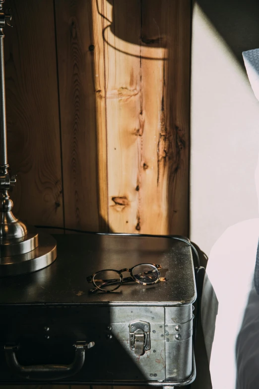 a suitcase sitting on top of a bed next to a lamp, a still life, trending on unsplash, wearing victorian brass goggles, in a cabin, silver silver glasses, detail shot