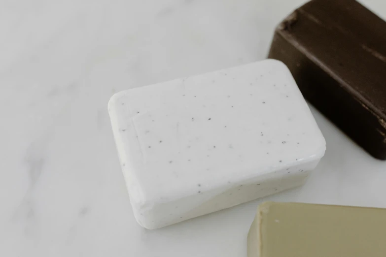a couple of soap bars sitting on top of a counter, inspired by Rachel Whiteread, white with chocolate brown spots, granite, detail shot, white