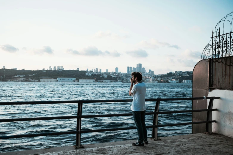 a person taking a picture of a body of water, by irakli nadar, pexels contest winner, hurufiyya, harbour in background, looking off to the side, a handsome, afternoon