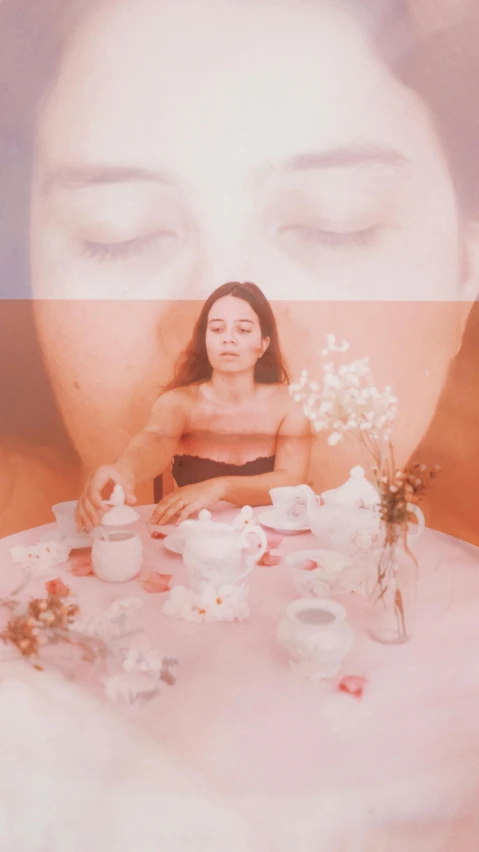 a woman sitting at a table with flowers in front of her, an album cover, tumblr, is ((drinking a cup of tea)), bella poarch, pastel faded effect, high quality photo