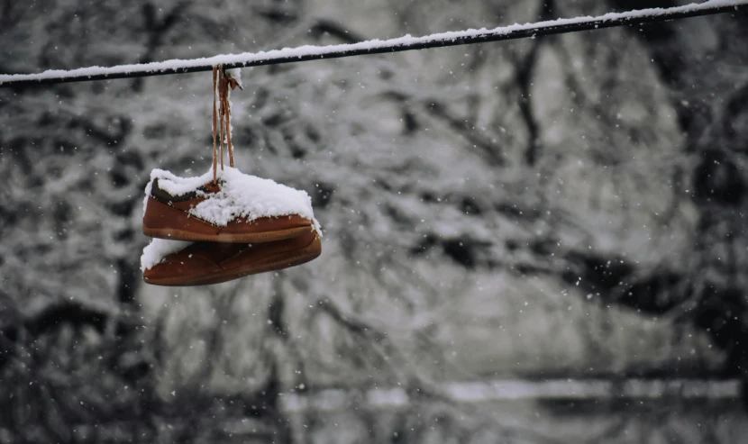 a pair of shoes hanging from a wire in the snow, by Alison Geissler, pexels contest winner, snowstorm ::5, brown, slippers, low light