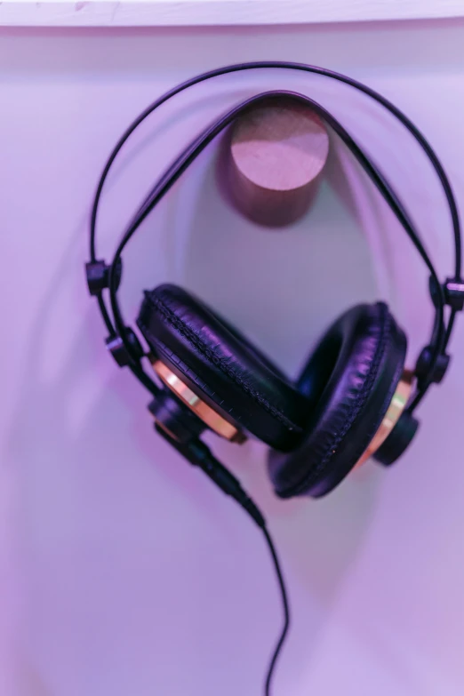 a pair of headphones hanging on a wall, by Niko Henrichon, trending on pexels, aestheticism, purple and gold color scheme, studio setup, black ears, vibrant.-h 704