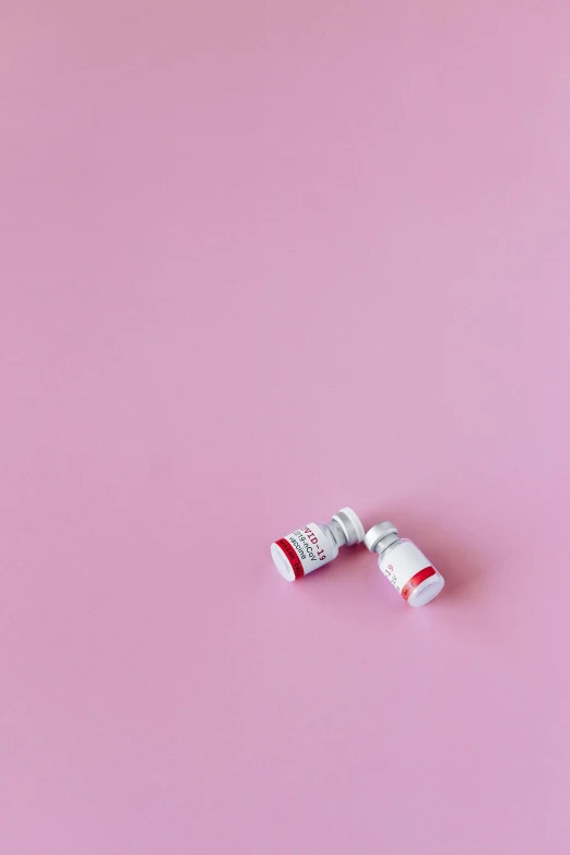 a couple of pills sitting on top of a pink surface, by Arabella Rankin, trending on pexels, visual art, blood collection vials, white and red color scheme, syringe, miniature product photo