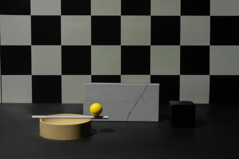 a yellow ball sitting on top of a table next to a black and white checkered wall, a still life, inspired by Bauhaus, made of carrara marble, tea ceremony scene, award-winning render, ceramic base