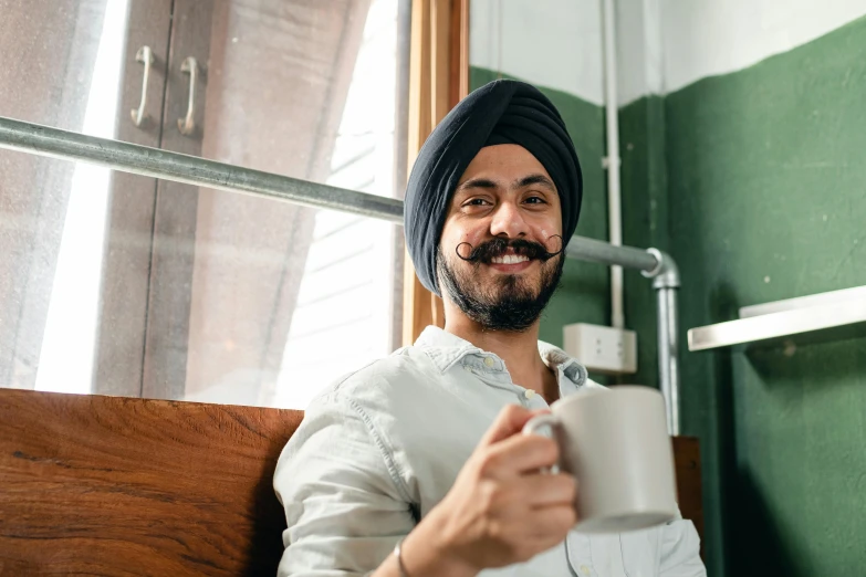 a man in a turban is holding a cup, inspired by Manjit Bawa, pexels contest winner, aussie baristas, relaxing and smiling at camera, avatar image, caring fatherly wide forehead