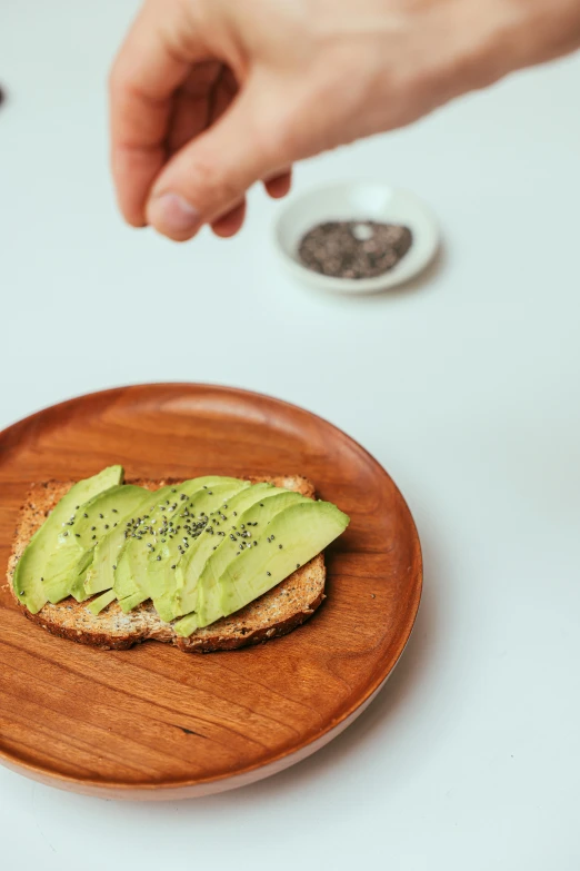 a person reaching for an avocado on a piece of bread, by Matthias Stom, pexels, on a wooden plate, detailed product image, jen atkin, hay