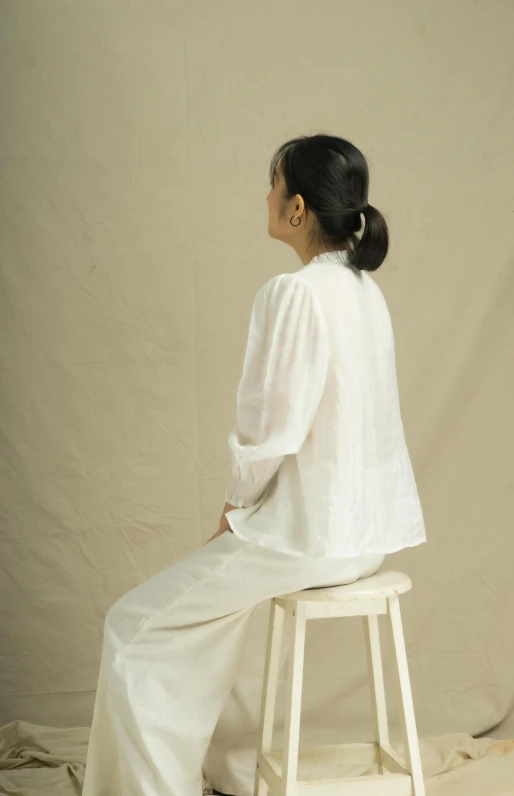 a woman sitting on top of a stool, inspired by Li Di, white wrinkled shirt, side view, wearing white pajamas, indonesia