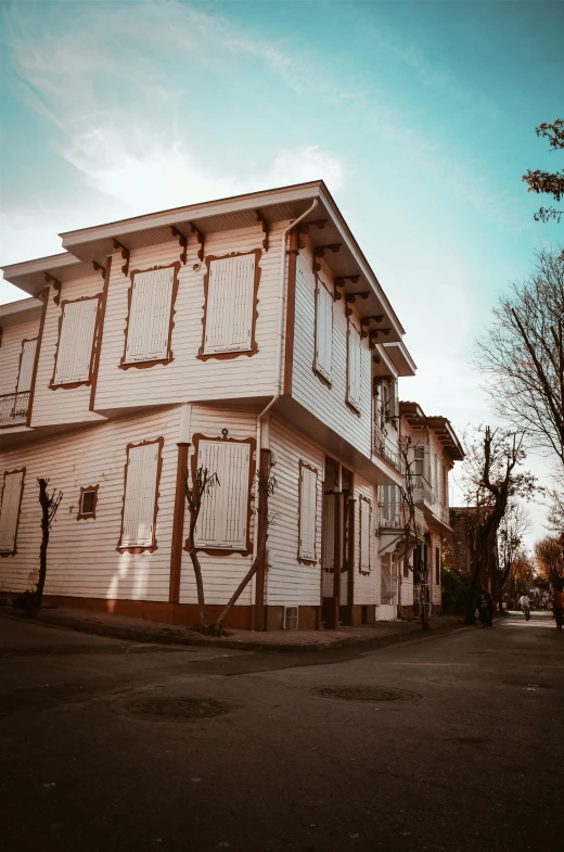 a large white building sitting on the side of a road, a colorized photo, inspired by Niyazi Selimoglu, pexels contest winner, art nouveau, peaceful wooden mansion, dramatic warm morning light, striped, turkey