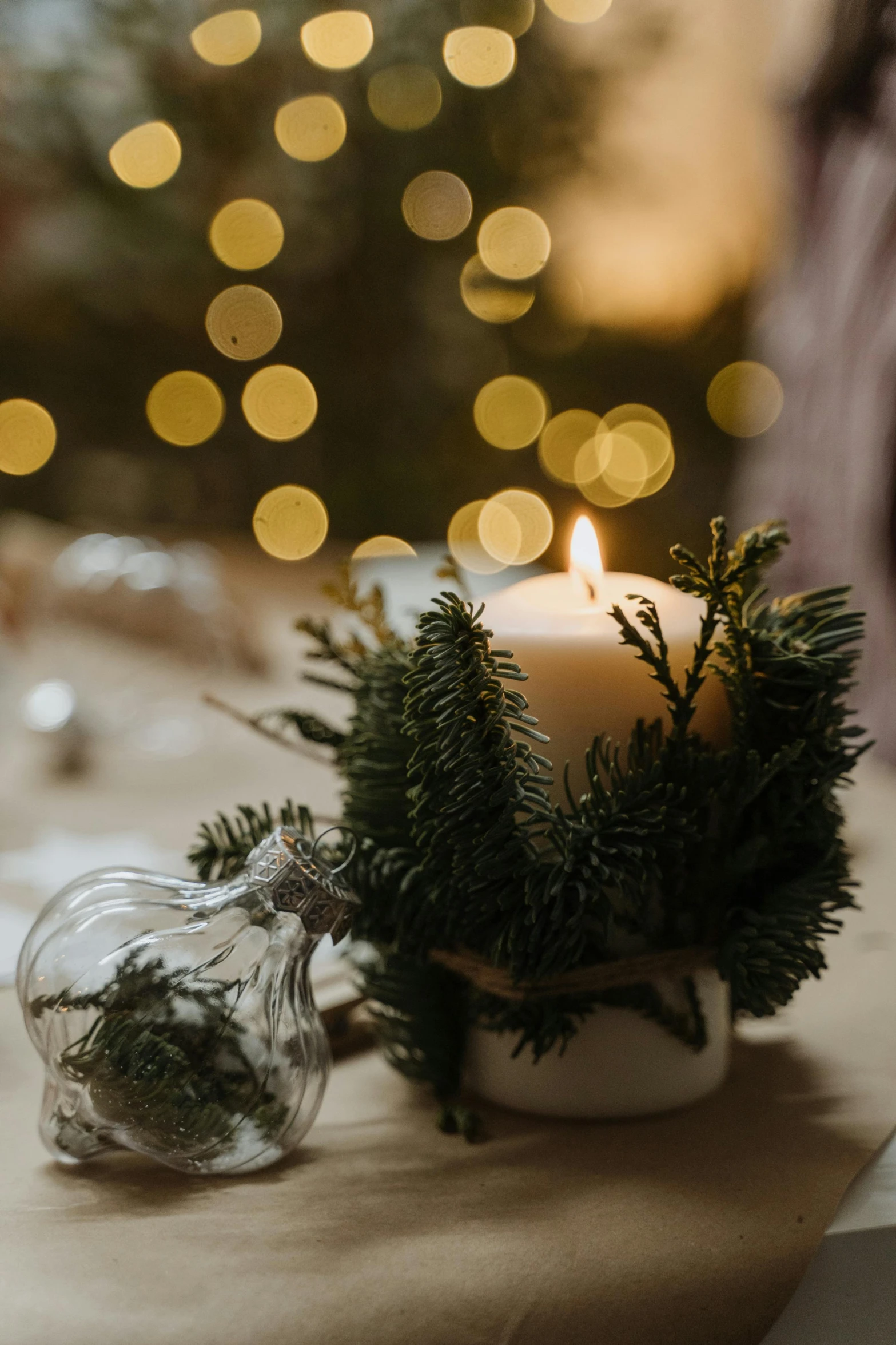 a candle sitting on top of a table next to a christmas tree, candlelit restaurant table, organic ornaments, softly lit, indoor setting