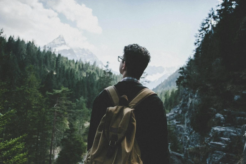 a man with a backpack standing in front of a mountain, pexels contest winner, trees in the background, profile pic, vintage vibe, looking up perspective