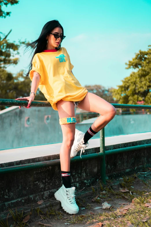 a woman in a yellow shirt is standing on a railing, inspired by Elsa Bleda, trending on pexels, happening, bra and shorts streetwear, wearing kneesocks, asian woman, doing a sassy pose