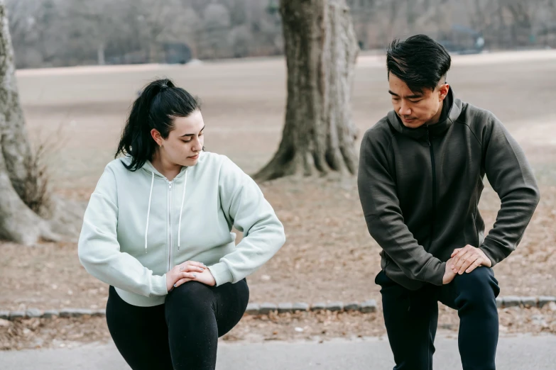 a man standing next to a woman on a skateboard, pexels contest winner, hunched over, wearing a tracksuit, sydney park, pixeled stretching