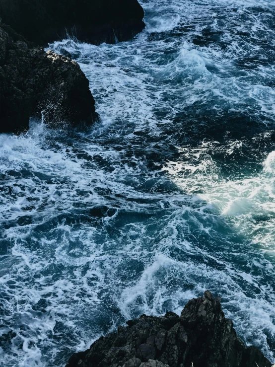 a man standing on top of a rock next to the ocean, an album cover, pexels contest winner, rushing water, deep texture, close-up from above, an eerie whirlpool