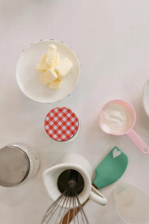 a table topped with bowls of food and a whisk, butter, detailed product image, soft white rubber, jars