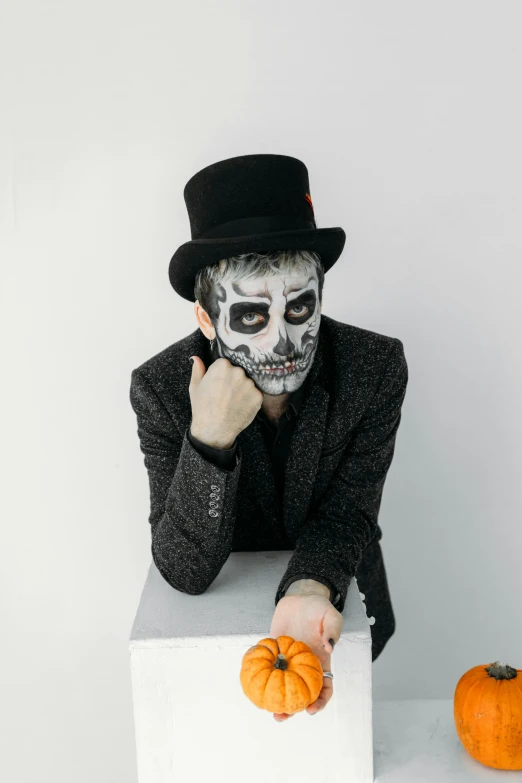 a man in a top hat is holding a pumpkin, inspired by James Bolivar Manson, pexels contest winner, lowbrow, skull face paint, on a white table, facepaint facepaint facepaint, promotional image