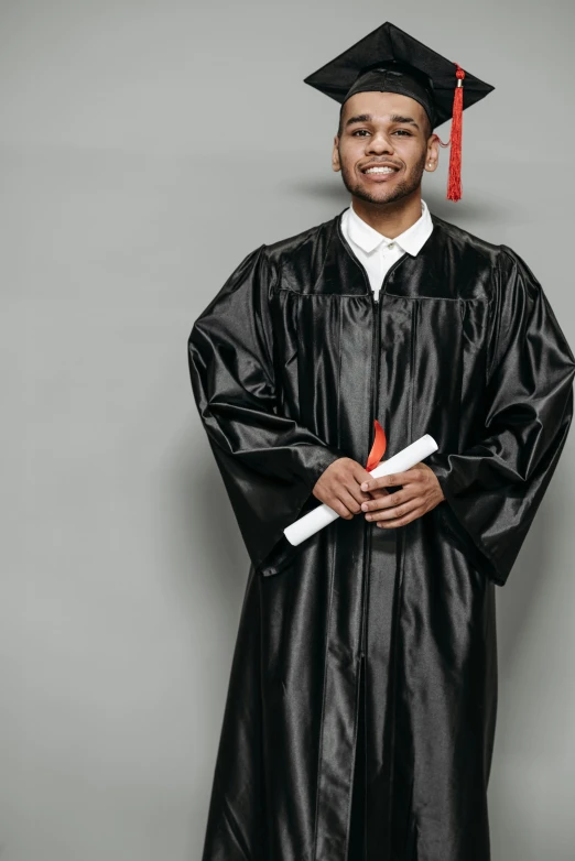 a man in a graduation gown holding a diploma, trending on pexels, black leather garment, backdrop, black teenage boy, standing straight