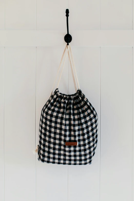 a black and white checkered bag hanging on a wall, by Helen Stevenson, bedhead, official product photo, idyllic, carrying big sack