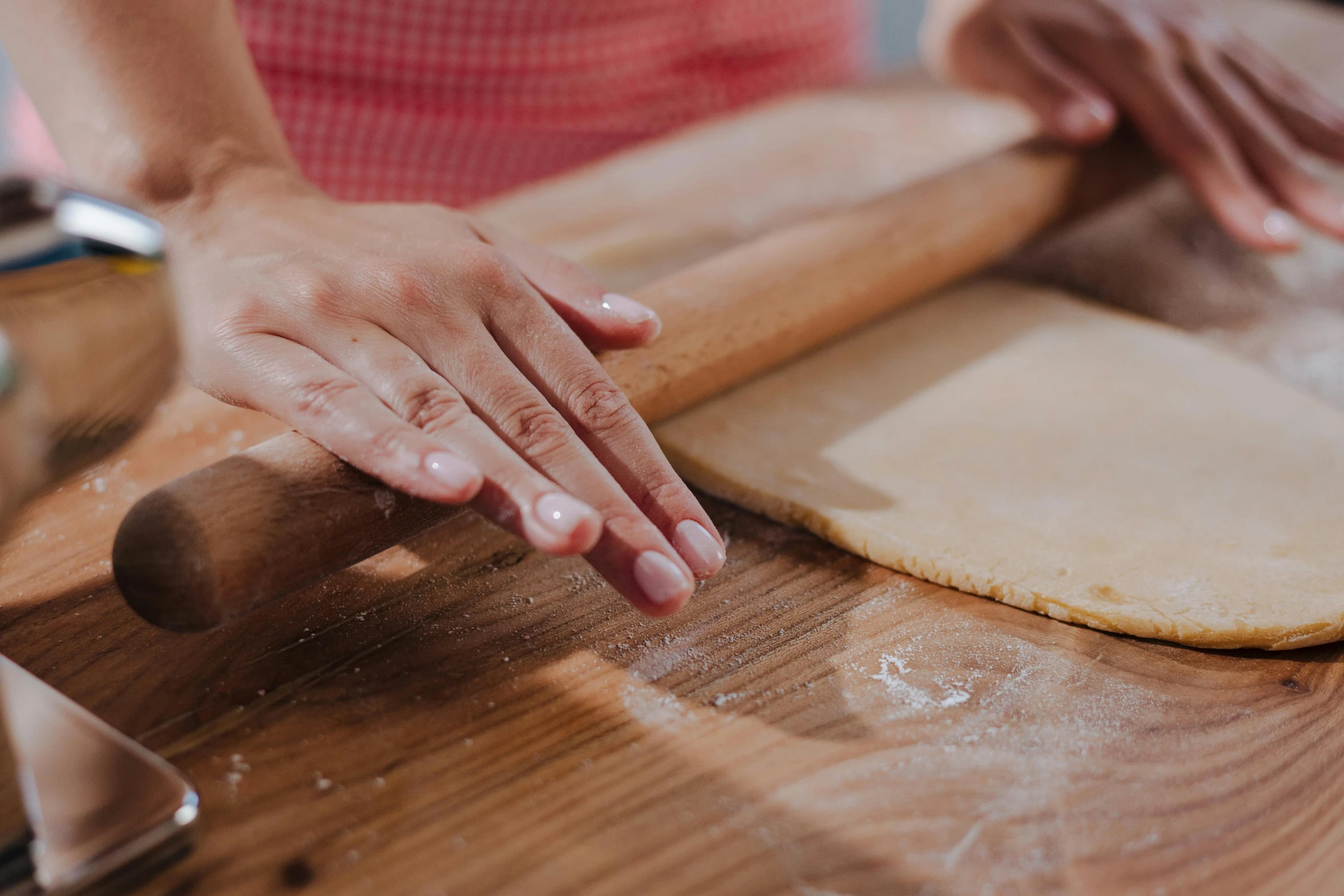 a person rolling out dough on a wooden table, by Julia Pishtar, trending on pexels, fan favorite, holding a staff, close together, dessert