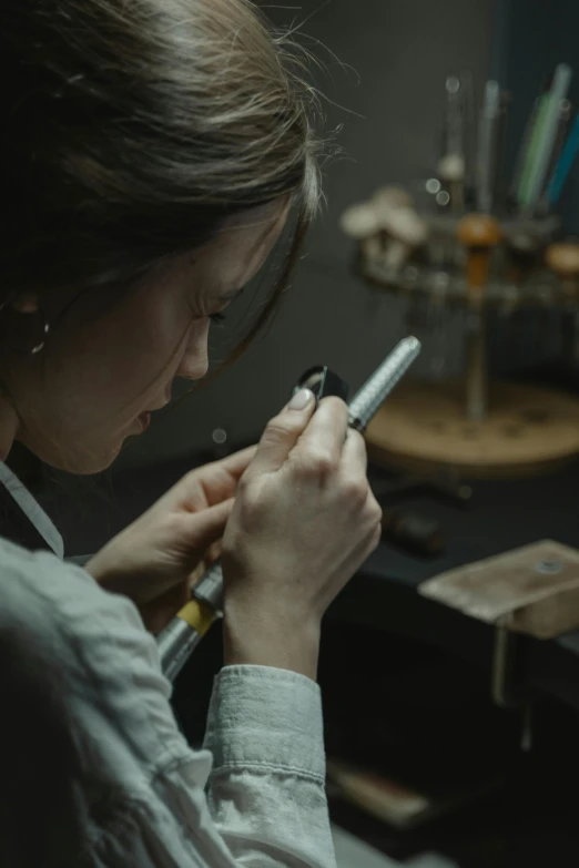 a woman is looking at her cell phone, an engraving, by Adam Marczyński, pexels contest winner, arbeitsrat für kunst, smoking soldering iron, closeup portrait of an artificer, color footage, chaumet