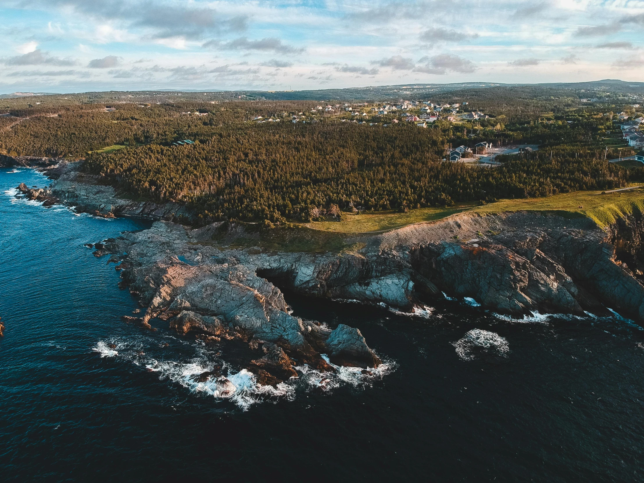 a large body of water next to a forest, by Doug Wildey, pexels contest winner, happening, coastal cliffs, drone view of a city, thumbnail, hziulquoigmnzhah