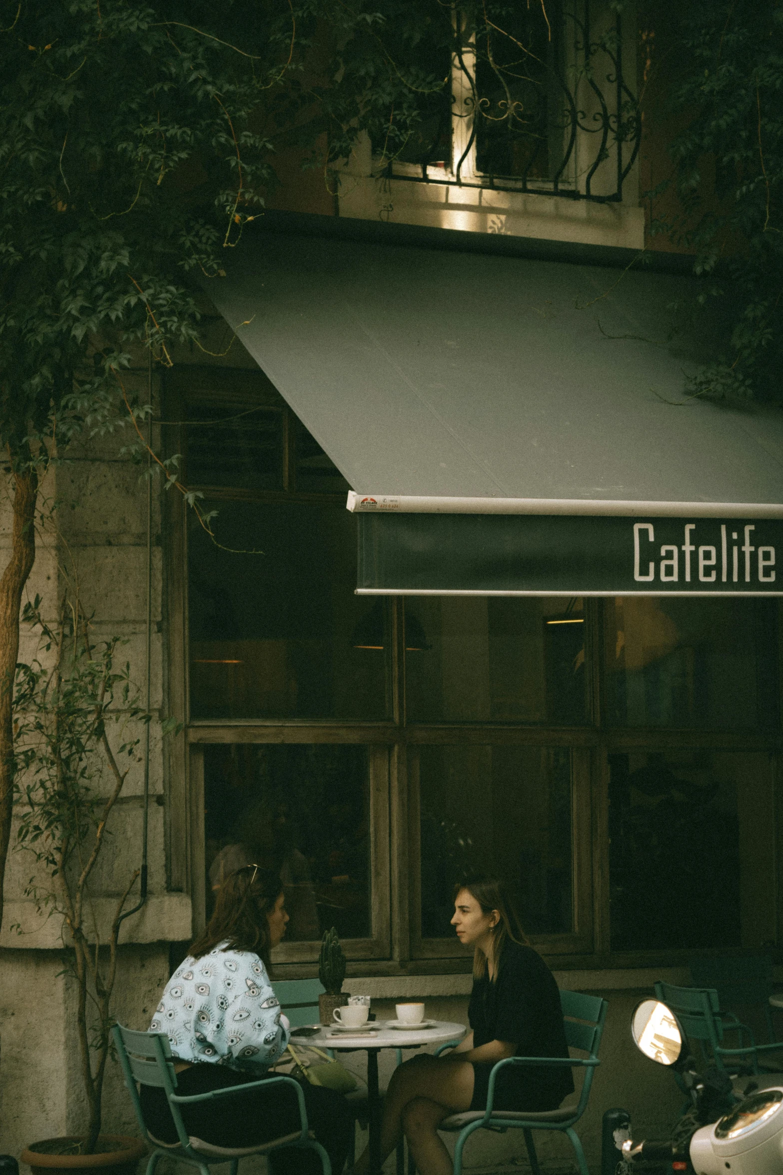 a couple of people sitting at a table in front of a cafe, a photo, by Elsa Bleda, unsplash contest winner, hyperrealism, awnings, commercial banner, canopee, tel aviv street