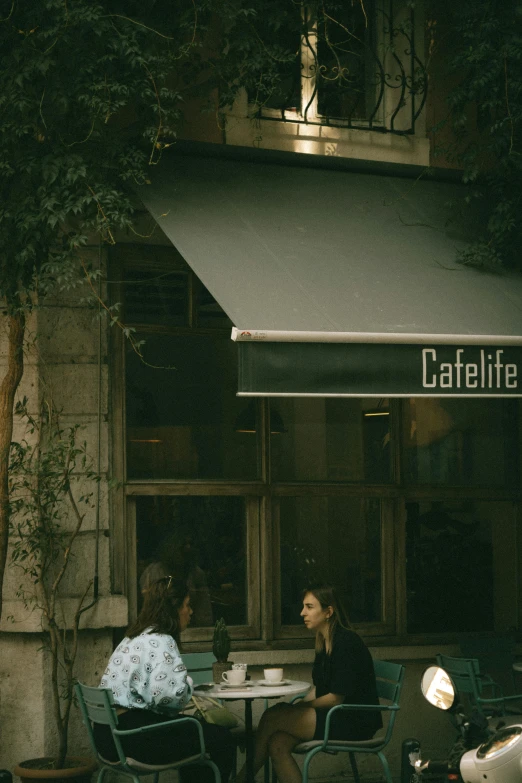 a couple of people sitting at a table in front of a cafe, a photo, by Elsa Bleda, unsplash contest winner, hyperrealism, awnings, commercial banner, canopee, tel aviv street