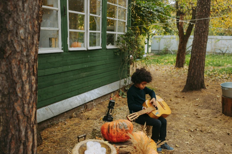 a person playing a guitar in front of a house, by Emma Andijewska, pexels contest winner, pumpkin patch, cute boy, childish gambino, rustic setting